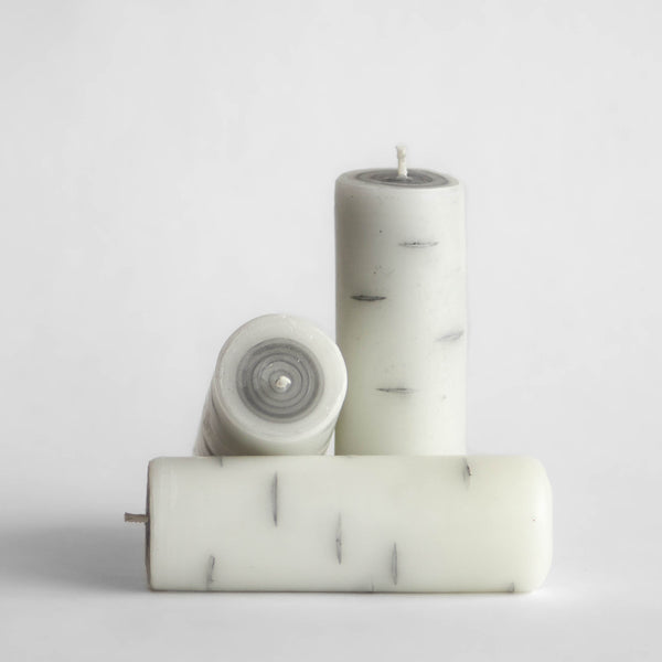 Photo of three tall Birch Log candles made of 100% Canadian beeswax, one standing upright and two on their sides, with white background.